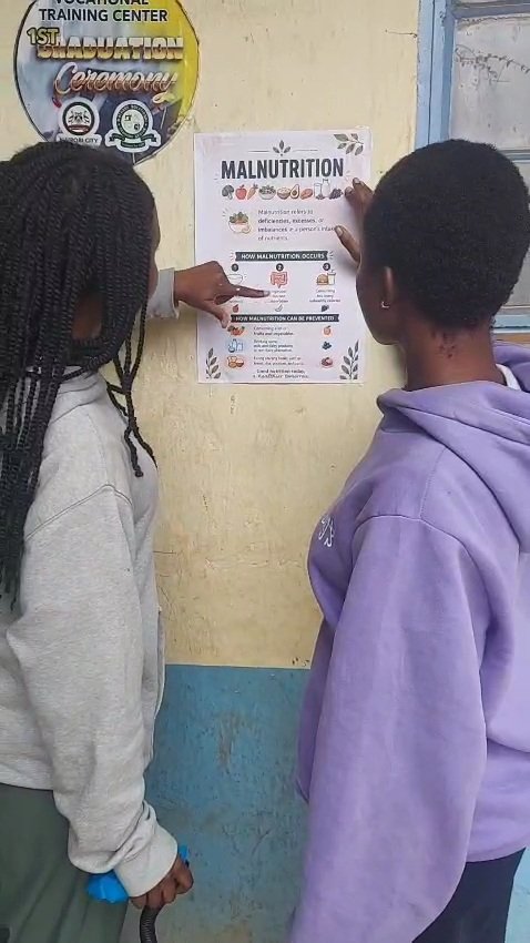 Two students putting up a poster about malnutrition on a wall at a partner site